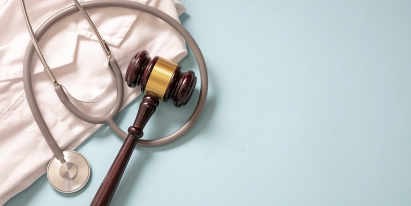 A stethoscope, doctor's coat, and gavel on a blue background, symbolizing medical malpractice and legal accountability.