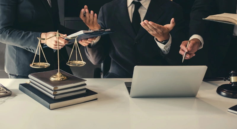 A group of lawyers using technology gathered around a table with a laptop.