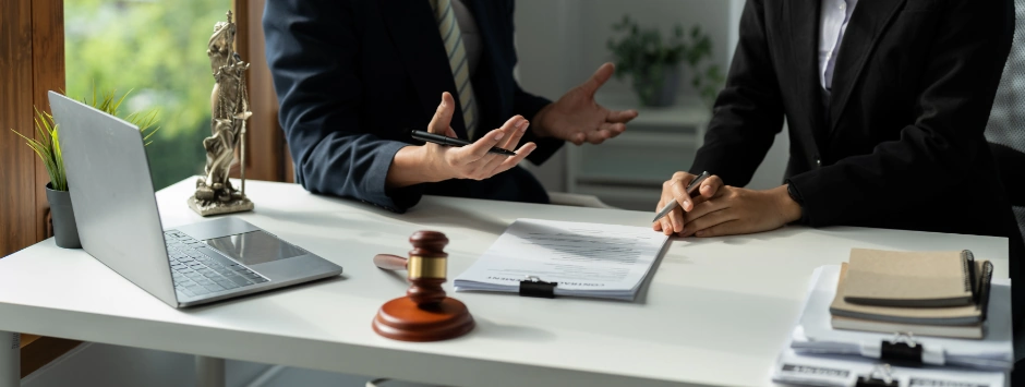 Criminal Attorney discussing legal strategy with a client at a desk featuring a laptop, papers, a gavel, and a small statue of Lady Justice.