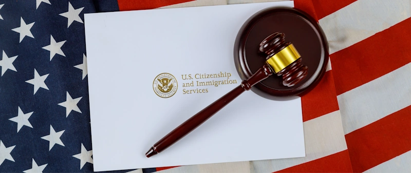 A gavel on a U.S. Citizenship and Immigration Services envelope over an American flag symbolizing the significance of hiring an immigration lawyer.