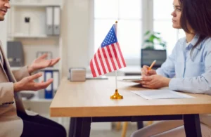 Two people at a desk with a small American flag in the middle highlighting the importance of hiring an immigration lawyer